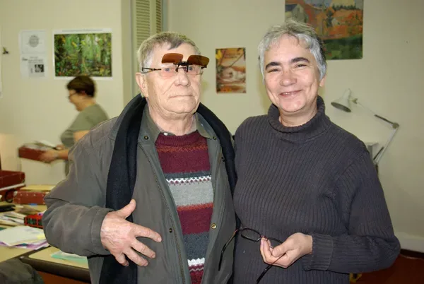 Un audiolecteur et une bénévole souriants, côte à côte, dans la bibliothèque.